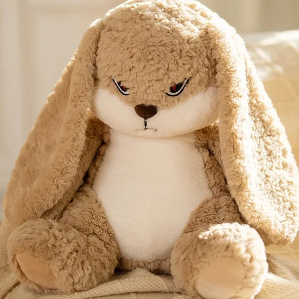 BunnyZ, conejo de peluche café con orejas largas, cara enojada y barriga blanca, sentado sobre una cama